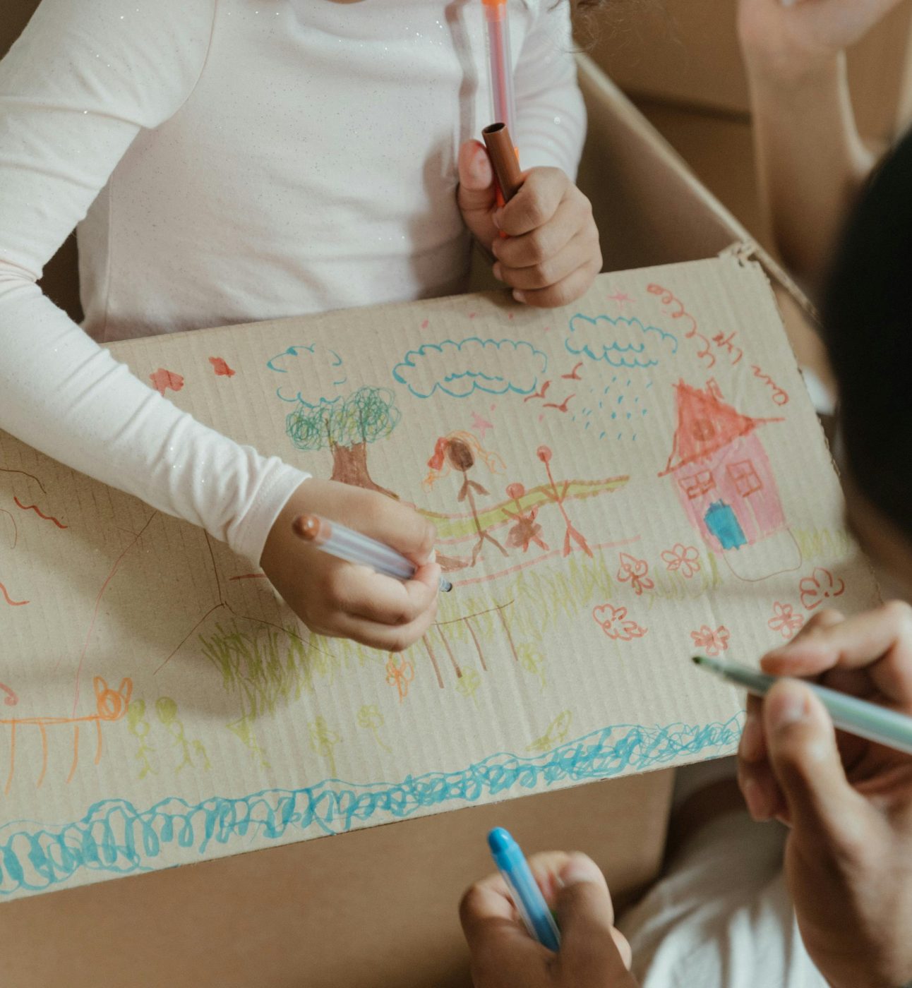 children drawing and painting picture of a house with flowers on a cardboard box